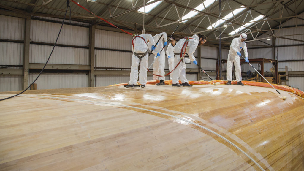5 people atop a large wooden upside down boat hull coat with large rollers