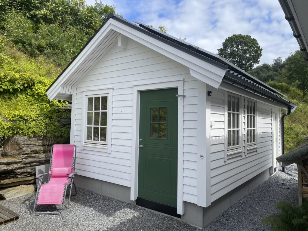 A hobbyist workshop built in a back garden. It's white with a dark green door and made from wood.