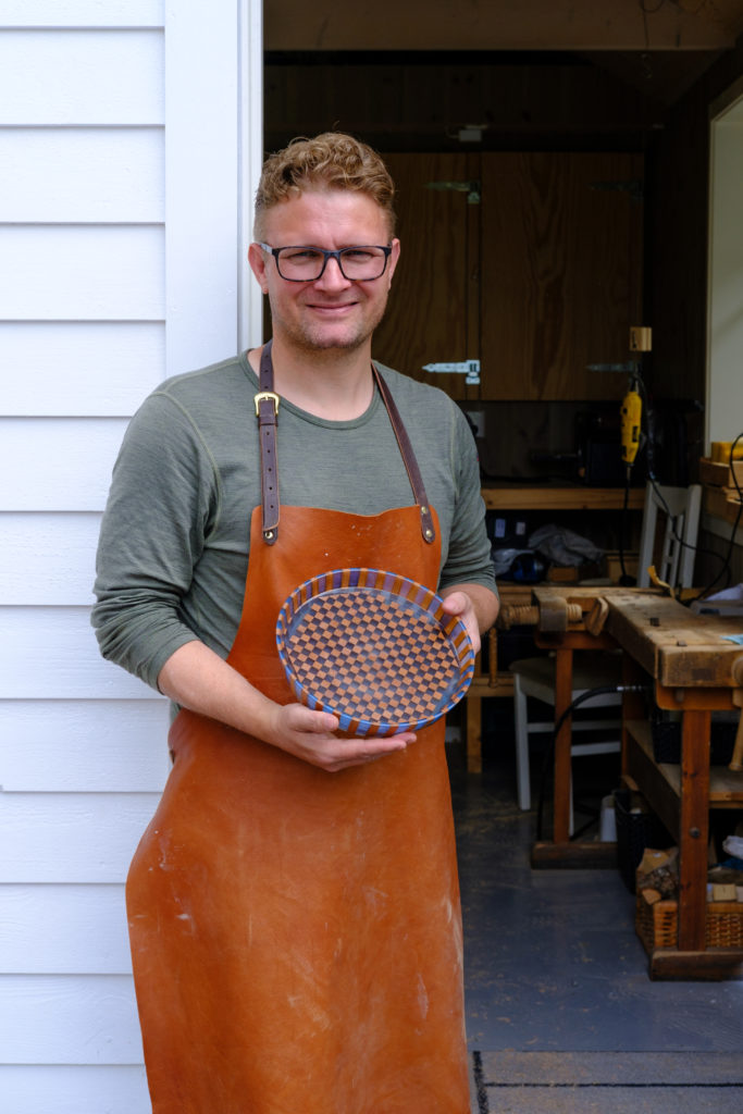 A person wearing an apron holding a bowl made from wood and epoxy resin.