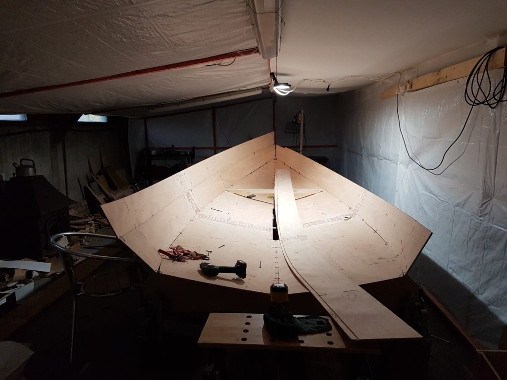 A dimly lit workshop with the cut out swallow yachts flat pack assembled into a boat and held together with west system epoxy