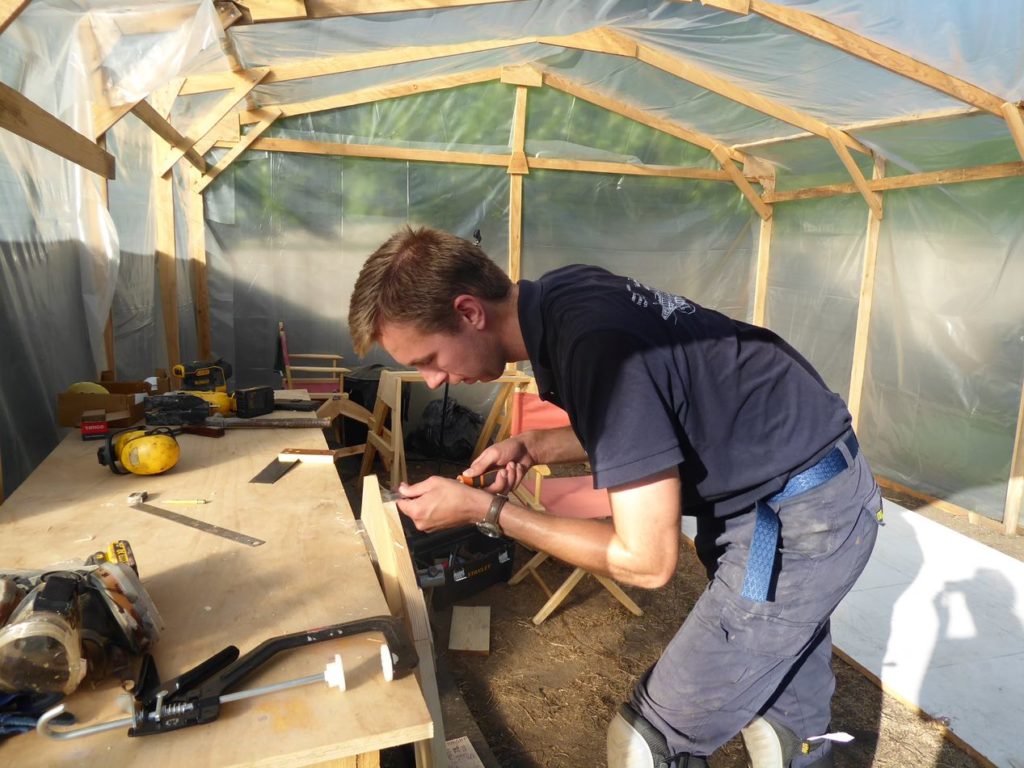 A man in his wooden workshop in the garden making a wooden dinghy with west system epoxy