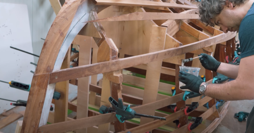 man working on his wooden boat, applying west system epoxy with a paintbrush