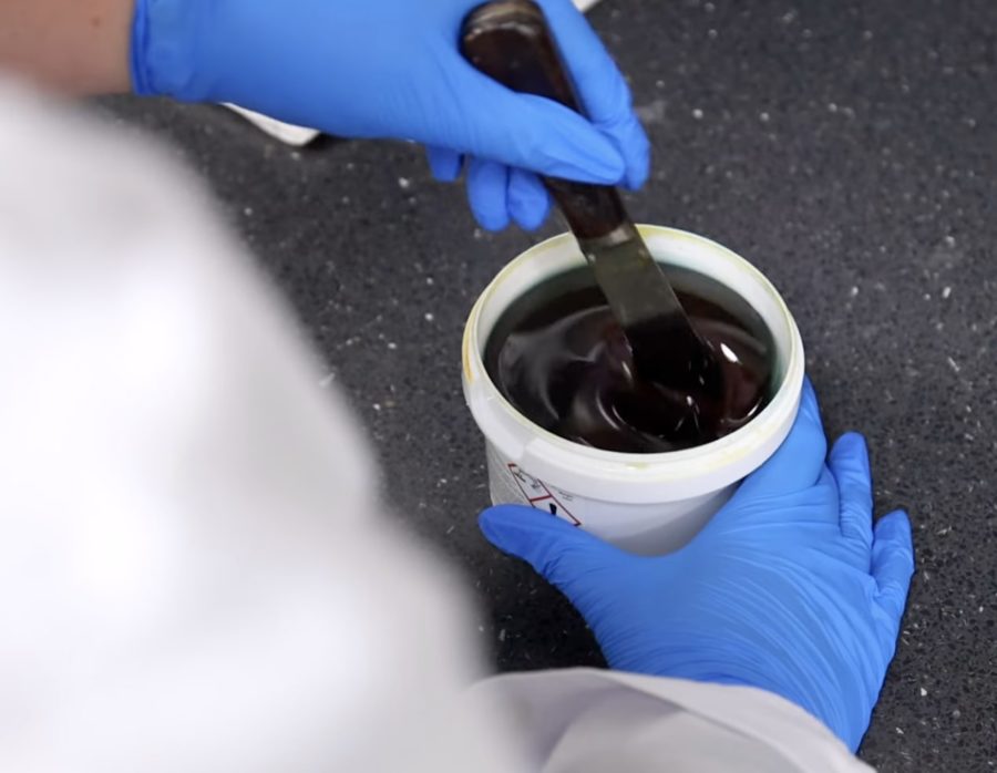 Person in lab coat stirs a thick dark liquid