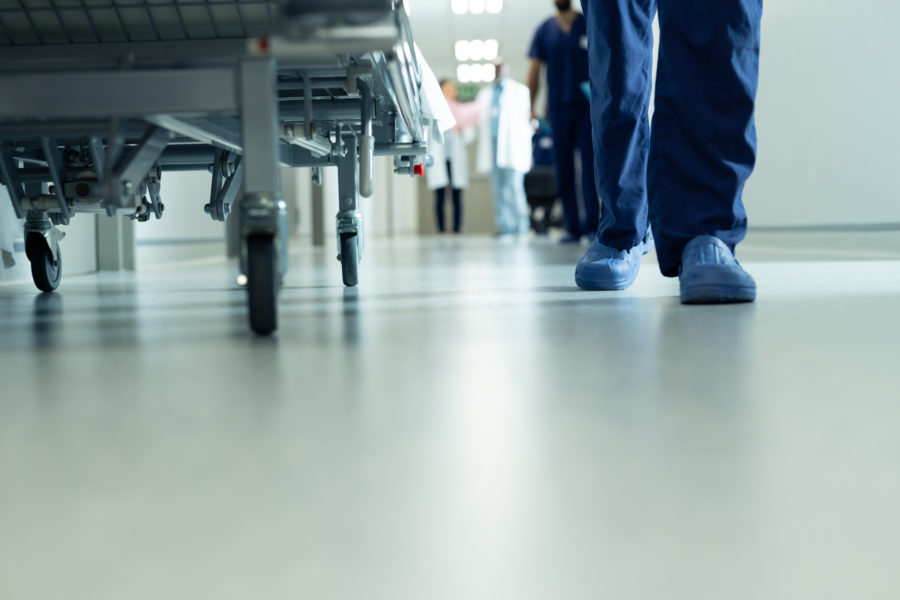 Low section of legs of hospital workers walking and hospital bed in corridor, with copy space. Hospital, medical and healthcare services.