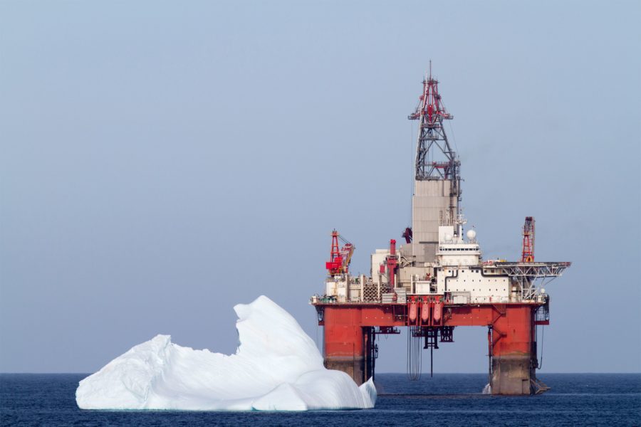 Offshore oil rig on the surface of blue water in the ocean with a floating iceberg.
